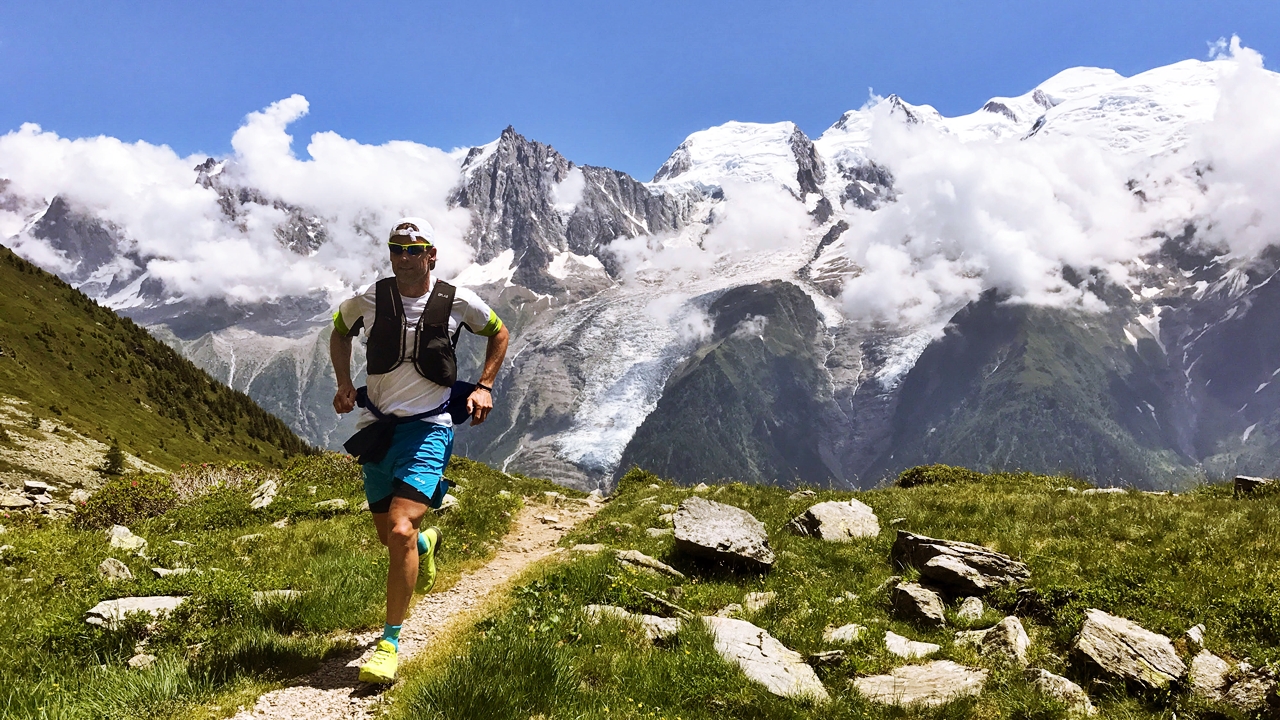 A man running on an alpine trail on a sunny day.